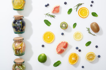 top view of detox drinks in jars near fruit slices, berries and herbs