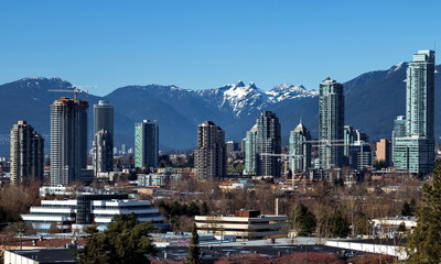 New residential area of  high-rise buildings in the city of Burnaby, construction site in the center of the city against the backdrop of snow covered mountain range and blue sky, Vancouver Canada