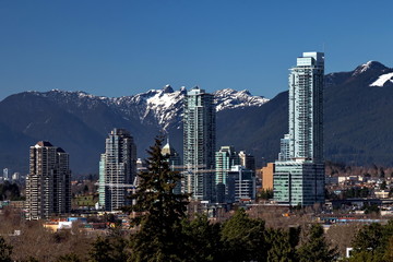 Fototapeta na wymiar New residential area of high-rise buildings in the city of Burnaby, construction site in the center of the city against the backdrop of snow covered mountain range and blue sky, Vancouver Canada