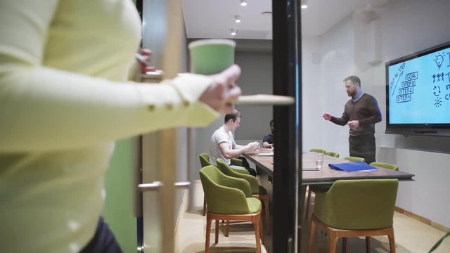Young woman being late for meeting with executive entering board room. Displeased manager repeating main points for her using digital board