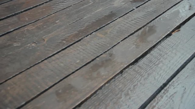 Old unpainted boards in the rain. The camera is moving. Raindrops crashing on wood flooring. April rain. Close-up. Nostalgic mood