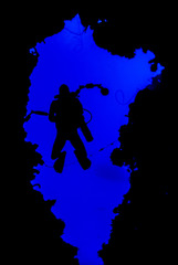 A silhouette shot of a scuba diver with an underwater camera in his hand descending into the abyss. The image is framed by a naturally occuring hole in the reef