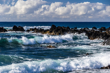 Waves rolling towads shore  near South Point, in Hawaii's Big Island. Volcanic rocks in the surf. Blue Pacific Ocean stretches to the horizon; overhead is a sky-filled sky.