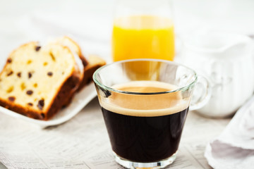 Continental breakfast table with cup of hot black coffee, milk, cakes and orange juice