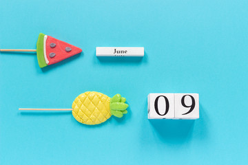 Wooden cubes calendar date June 9th and summer fruits candy pineapple, watermelon lollipops on...