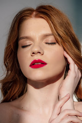 beautiful young redhead woman with red lips posing with eyes closed