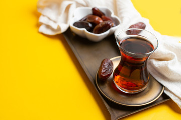 Ramadan Kareem Festival, close up of dates at bowl with rosary and cup of black tea on yellow background.