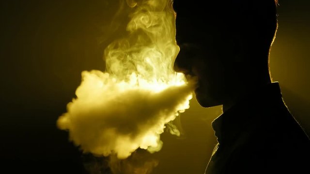 Silhouette of vaping man in the darkness. Boy blowing O's with vapor from e-cigarette. Vape tricks