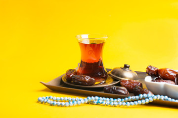 Ramadan Kareem Festival, Dates on wooden bowl with cup of black tea and rosary on yellow background