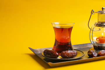 Ramadan Kareem Festive, close up of dates on plate with oriental candle lamp and cup of black tea on yellow background.