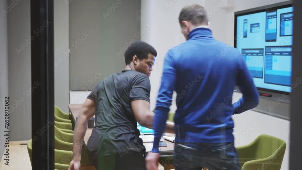 Wall mural manager entering meeting room, greeting web designer with handshake and looking at website templates