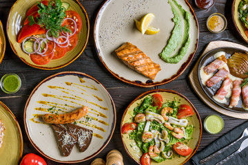 salmon steak, vegetable salad, pork sausages, seafood salad and grilled bacon with cheese