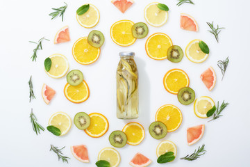 flat lay with sliced kiwi, oranges, lemons, grapefruits, mint, rosemary and detox drink in bottle on grey background