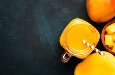 Freshly squeezed fresh mango juice in large glass jar with fresh fruit on dark blue background,...