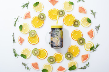 flat lay with sliced kiwi, oranges, lemons, grapefruits, mint, rosemary and detox beverage in jar on grey background