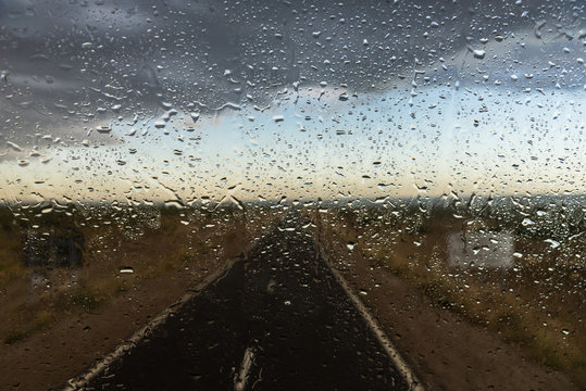 Water drops against the background of a highway road with rain dark clouds, steppes, and mountains