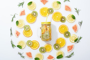 flat lay with sliced kiwi, oranges, lemons, grapefruits, mint, rosemary and detox drink in jar with straw on grey background