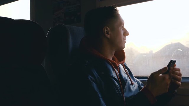 Young man having train journey. Man looking out the window during train ride at sunset