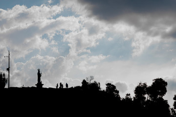 silhouette of the top of a hill where is a statue of the holy mary and a group of people