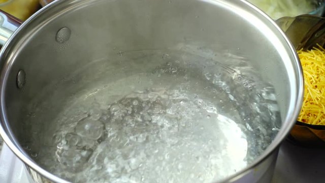 Add salt to boiling water in a metal pan close-up.