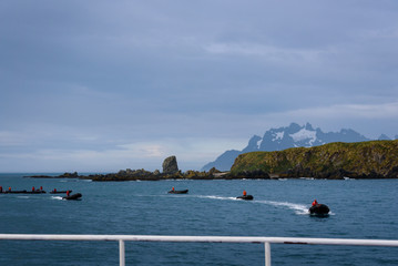 View of Coopers Bay landscape from cruise ship, fleet of inflatable rafts with drivers in red jackets getting ready to pick up tourists off ship, South Georgia, southern Atlantic Ocean