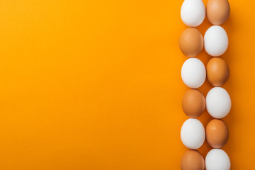 top view of white and brown organic chicken eggs on bright orange background with copy space