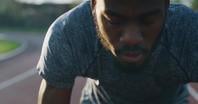 Slow motion close up of young african male athlete is launching off the start line in a race in athletics stadium.