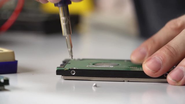electronic engineer repairs computer hard drive. technologist with a screwdriver disassembles hdd