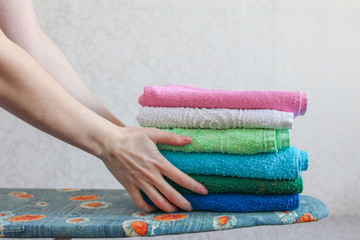 Stack of colorful clean towels  on grey background. Ironing clothes on ironing board. Stack of...