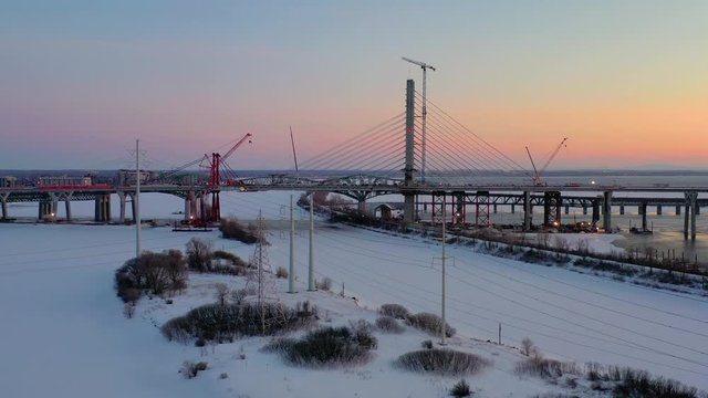 A slow moving aerial shot at twilight that flies over a half-frozen river, showing a long bridge and a brightly city in the background
