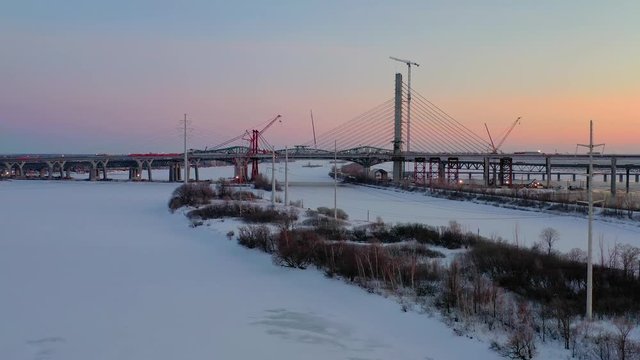 A slow moving aerial shot at twilight that flies over a half-frozen river, showing a long bridge champlain and a brightly city in the background