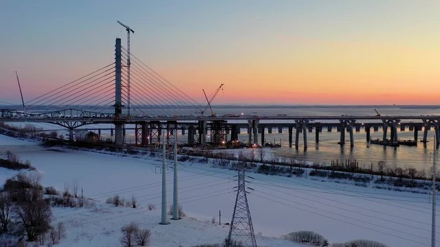 A slow moving aerial shot at twilight that flies over a half-frozen river, showing a long bridge and a brightly city in the background