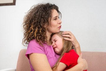 A young mother calms her little daughter.  The girl is crying and her mother hugged her with love,