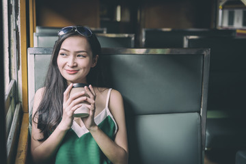 Asian woman traveler has drinking coffee in the train with happiness at Hua Lamphong station at Bangkok, Thailand.