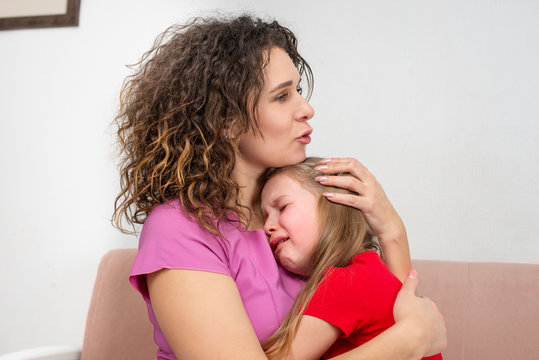 A young mother calms her little daughter.  The girl is crying and her mother hugged her with love,