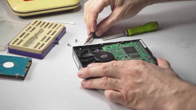 electronic engineer repairs computer hard drive. technologist with a screwdriver disassembles hdd