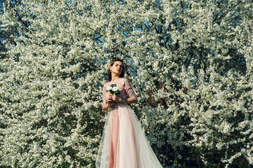 Portrait of a young beautiful fashionable woman in an evening dress . Girl posing in a blooming...