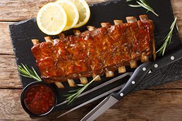 Traditional barbecue pork ribs served with spicy sauce and lemon close-up table. horizontal top view