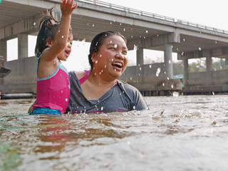 Little Asian baby girl, 25 months old, enjoys playing water in a river with her auntie - playing...