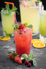Cold strawberry drink on textured gray table. Lemonade pitcher and two glasses of fruit juice  at the background out of focus.