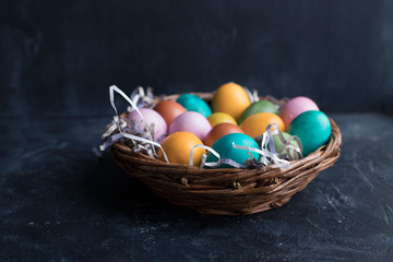 Colorful Easter eggs in basket on black wooden background with copy space.