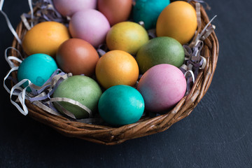 Colorful Easter eggs in basket on black wooden background with copy space.