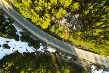 Old asphalt road in the spring forest top view Snow melts on the side of the road and between the trees.