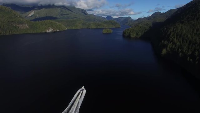 Aerial: White Motorboat Driving Towards Forest Covered Mountains in Mackenzie Sound, British Columbia