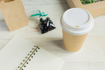 Open Notebook and brown paper craft cup of coffee to go on white wooden table