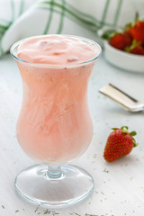 Pink strawberry mousse in goblet glass on white wooden background with text space.