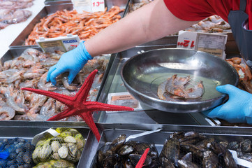 he seller in blue gloves puts the fresh  king prawns in an iron bowl on the fish market