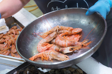 the seller in blue gloves puts the king prawns in an iron bowl on the market