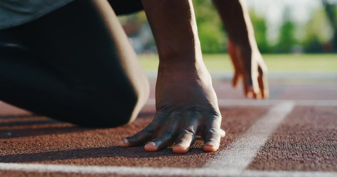 Slow motion close up of young african male athlete is launching off the start line in a race in athletics stadium.