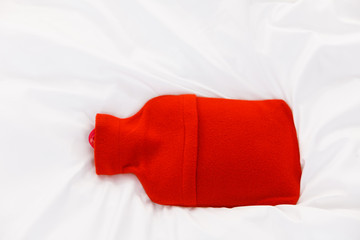 Warm red hot water bottle on white bedding